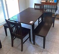 Side angle photo showing dark wood dining table with two matching chairs and two benches.