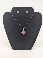 Necklace with pendant and matching stud earrings displayed on black jewelry bust.