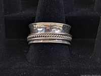 Front view of the spinner ring on a black ring stand showing hammered silver band and twisted rope spinner.