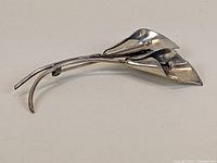 Front angled view of a sterling silver cala lily flower brooch showing two flowers with smooth petals and round centers.