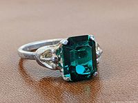 Front view of a sterling silver ring with large green emerald-cut stone, showing the setting and band.