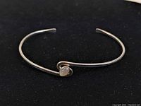 Sterling silver cuff bracelet with round moonstone cabochon set on one side, shown on black background from a front angle.