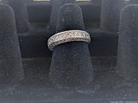 Sterling silver band ring displayed on a black ring holder showing the front and side views, highlighting the rows of clear stones and textured design.