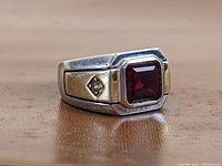 Angle view of men's sterling silver ring displaying the large square red stone and gold plated side panel with embedded clear stone.