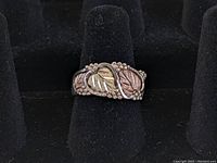 Front view of the sterling silver ring displaying rose and yellow gold leaf inlays with vine and berry design, shown on black ring stand.