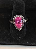 Close-up photo of the sterling silver ring showing the pear-shaped pink central stone surrounded by smaller clear stones on a black display stand.