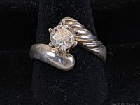 Close-up photo of sterling silver solitaire ring showing twisted band and clear faceted stone mounted with six prongs, displayed on black velvet ring holder.