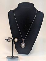 Photo of the sterling silver puffy oval earrings and matching pendant displayed on a black necklace bust and earring stand. Pendant hangs on the chain.