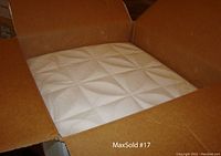 Open box showing stacked white ceiling tiles with geometric embossed pattern inside a cardboard box.