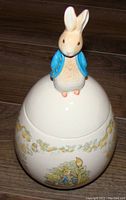 Front view of ceramic egg container with Peter Cottontail bunny figure lid showing painted details and floral decoration on body.