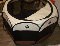 Brown and cream foldable pet playpen with black mesh sides and paw print design. Zippered mesh door visible, standing set up on floor.