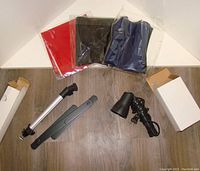 Red, black, and blue fabric backdrops packaged unused, alongside tripod light parts on wood floor.