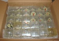 30 wine stoppers in a cardboard box laid out in a grid, each with plastic packaging showing the colorful round top design.