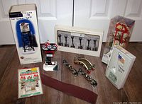 Full view of assorted Department 56 holiday village accessories including boxed Harley Davidson water tower, motorcycle sign, street lights, brick pathway rolls, and American flag light box.