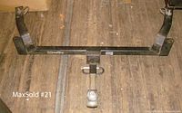 Full view of the black metal Draw-Tite tow bar laid horizontally on a wooden floor, showing the overall frame and drop hitch attachment.