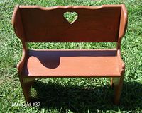 Front view of wooden child's bench with heart cutout in backrest, showing overall condition and shape.