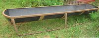 Side view showing the full length of the 10-foot livestock feeder on metal legs with rust and black plastic trough.