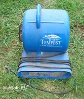 Side front view of blue Tempest Dry Air Machine showing handle, logo and coiled power cord.