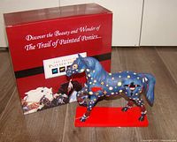 Trail of Painted Ponies box with the blue painted pony figurine on red base, showing front-left side with painted symbols and box behind.