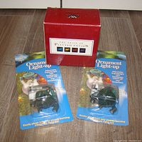 Lot contents showing original box for Painted Ponies ornament and two Roman light-up ornament spotlight lights in blister pack packaging.
