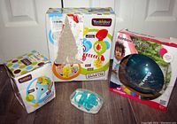 Lot showing Yookidoo Fun Elefun Fill N Sprinkle Water Lab box with some damage to front, Rainbow Soft Ball boxed toy, pacifiers in clear case, and another Yookidoo boxed item.