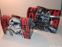 Two Star Wars-themed cardboard lunch boxes, one featuring Darth Vader and one with a Stormtrooper design, stacked and showing front and side views.