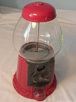 Full view of vintage red metal gumball machine with glass globe and coin dispenser on front