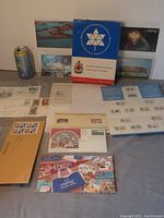 Wide view showing collection of stamps, first day covers, postcards, pamphlets, and envelopes arranged with a soda can for scale.