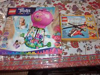 Photo showing the unopened boxes of Lego Trolls World Tour hot air balloon set and Creator Air Blazer Helicopter set on a patterned surface.