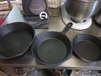 Three graduated cast iron fry pans displayed on a stainless steel countertop with their original box and care instruction sheet in the background.