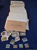 Multiple white and brown envelopes labeled with Canadian years and grouping (e.g., 1967) containing used Canadian postage stamps. Some loose stamps are displayed showing various Canadian stamp designs from different years.