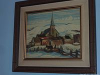 Framed print showing a winter scene of a church and buildings under a blue sky with clouds, featuring snow and fences