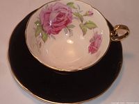 Top-down view showing pink rose floral design inside cup and solid black saucer with gold rim.