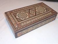 Rectangular antique wooden box with intricate marquetry geometric patterns and mother of pearl inlay on the corners and edges.