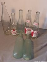 Photo showing seven vintage glass bottles. Four pop bottles with Towne Club and Diamond Supreme labeling and three green round bottom bottles. Bottles display general wear and tear.