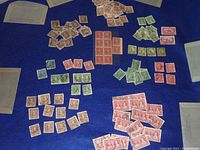 Wide shot showing a large assortment of red, green, and brown Canadian stamps laid out on blue surface, including blocks and some singles