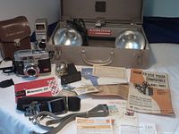 Photo showing Kodak cameras, instruction booklets, strap, and lighting components on table.