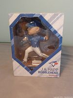 Front view of boxed J.A. Happ bobblehead showing the figure in pitching pose, packaged in original window display box with Toronto Blue Jays logos and Honda branding.