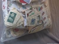 Close-up image showing diverse assortment of used stamps including green royal emblem stamps with cancellation marks, stamps with portraits, and multicolored stamps mounted on paper.