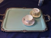 Topview of large silver plated serving tray with pale blue painted surface with two floral tea cups on it for scale