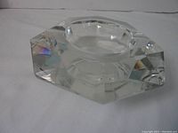 Angled photo showcasing the octagonal geometric shape of clear crystal ashtray with faceted sides and round bowl center, sitting on a white surface.