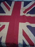 Full view of vintage Union Jack flag showing central red cross and white background with blue segments, fabric shows creasing and color variations due to wear.