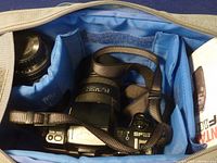 Top view inside the travel bag showing the Pentax camera with standard lens attached and the telephoto zoom lens secured in separate compartments with the instruction manual.