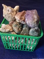 A green basket filled with large rough rocks and a purple amethyst crystal cluster on top.