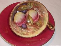 Cup placed inside saucer showing interior hand painted orchards and matching burgundy saucer, gold trim visible
