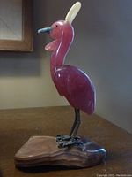 Side view of semi-precious stone bird with purple body, white feathers on head, metal legs, and stone base.