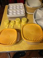 Photo showing 2 white Tupperware egg trays, 4 yellow measuring cups, and 2 yellow lidded square bowls with sunburst pattern on lids.