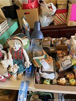 View of fabric dolls, lamp, framed items, silver cups, and assorted decor on table near cardboard and gift bags