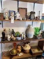 Shelves filled with assorted ceramics, glass jars, metal owl sculpture, vintage decor, and empty decorative frames.