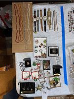 Full view of assorted costume jewelry laid out on towel including watches, pins, necklaces, earrings, and other pieces